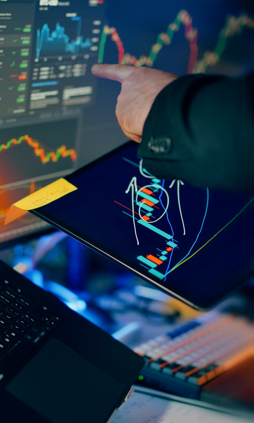Mano che indica grafici finanziari su un monitor.